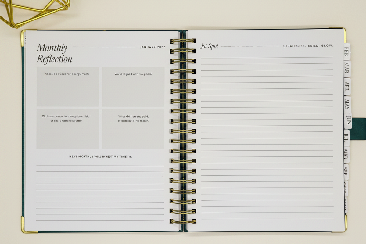 2027 Planner open to two-page  monthly reflection spread in spacious 7.5 x 10 format with tabbed months, coil binding, and styled alongside a gold geometric decor.
