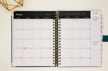 2027 Planner open to two-page monthly spread in spacious 7.5 x 10 format with tabbed months, coil binding, and styled alongside a gold geometric decor.