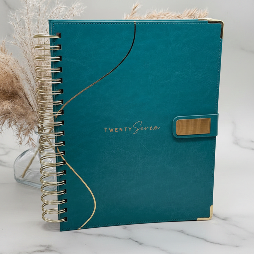 2027 Planner closed cover showcasing PU leather finish, reinforced corners, and magnetic closure, styled alongside feather decor. Marble Background.
