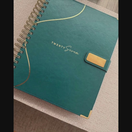 2027 Planner product showcase video with voiceover and on-screen text, featuring photos of the planner, teal bookmark, exterior and interior spreads, and a person in a white long sleeve blazer holding the planner.  