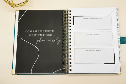 2027 Planner open to  the goal setting page, with tabbed months, coil binding, and styled alongside a gold geometric decor.
